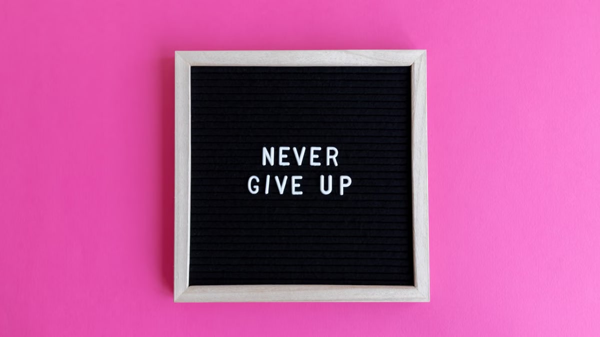 A framed letter board with 'NEVER GIVE UP' on a vibrant pink background.